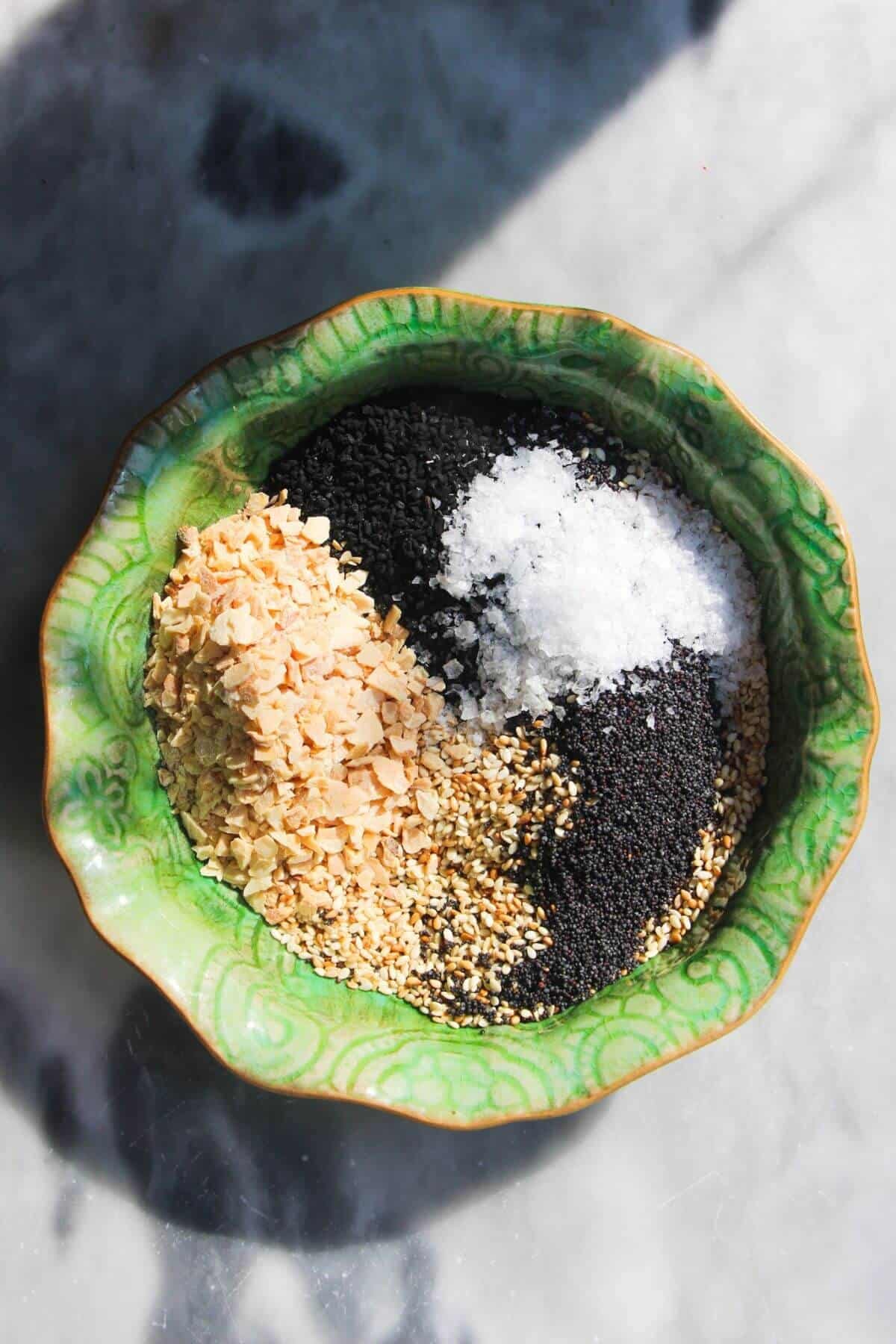 Ingredients for everything bagel seasoning in a small green bowl.