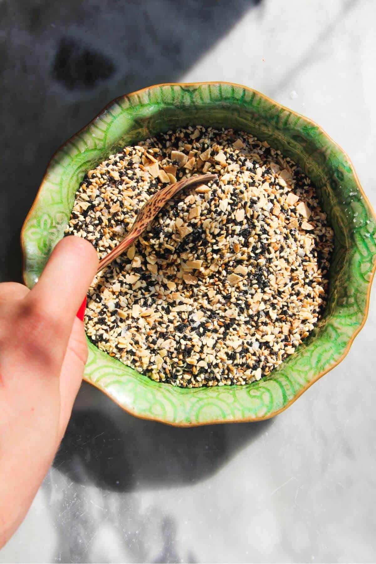 Spoon mixing everything bagel seasoning in a small green bowl.