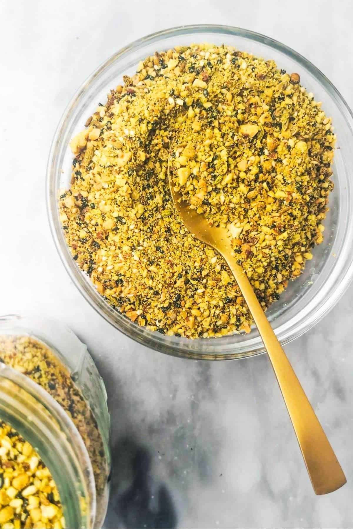 Dukkah in a small glass bowl with a jar on the side.