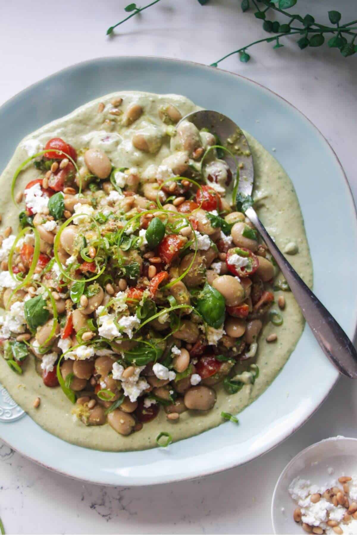 Mediterranean white bean salad on whipped basil tahini on a large light blue serving plate.