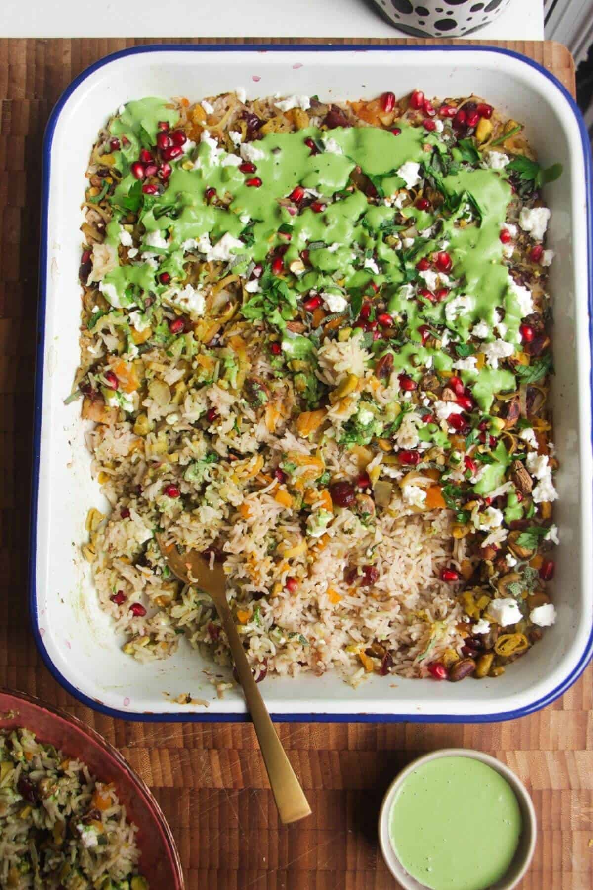 Spoon in baked rice topped with feta, pomegranate seeds and green tahini sauce.