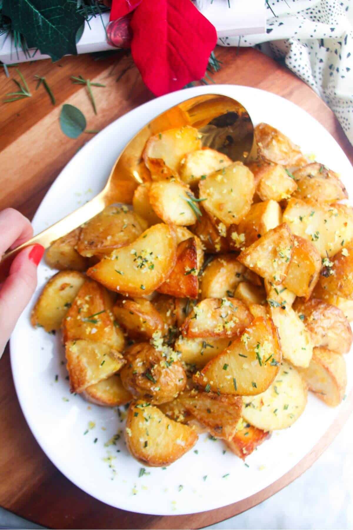 Crispy golden potatoes on a white oven plate with large gold spoon on a wooden background.