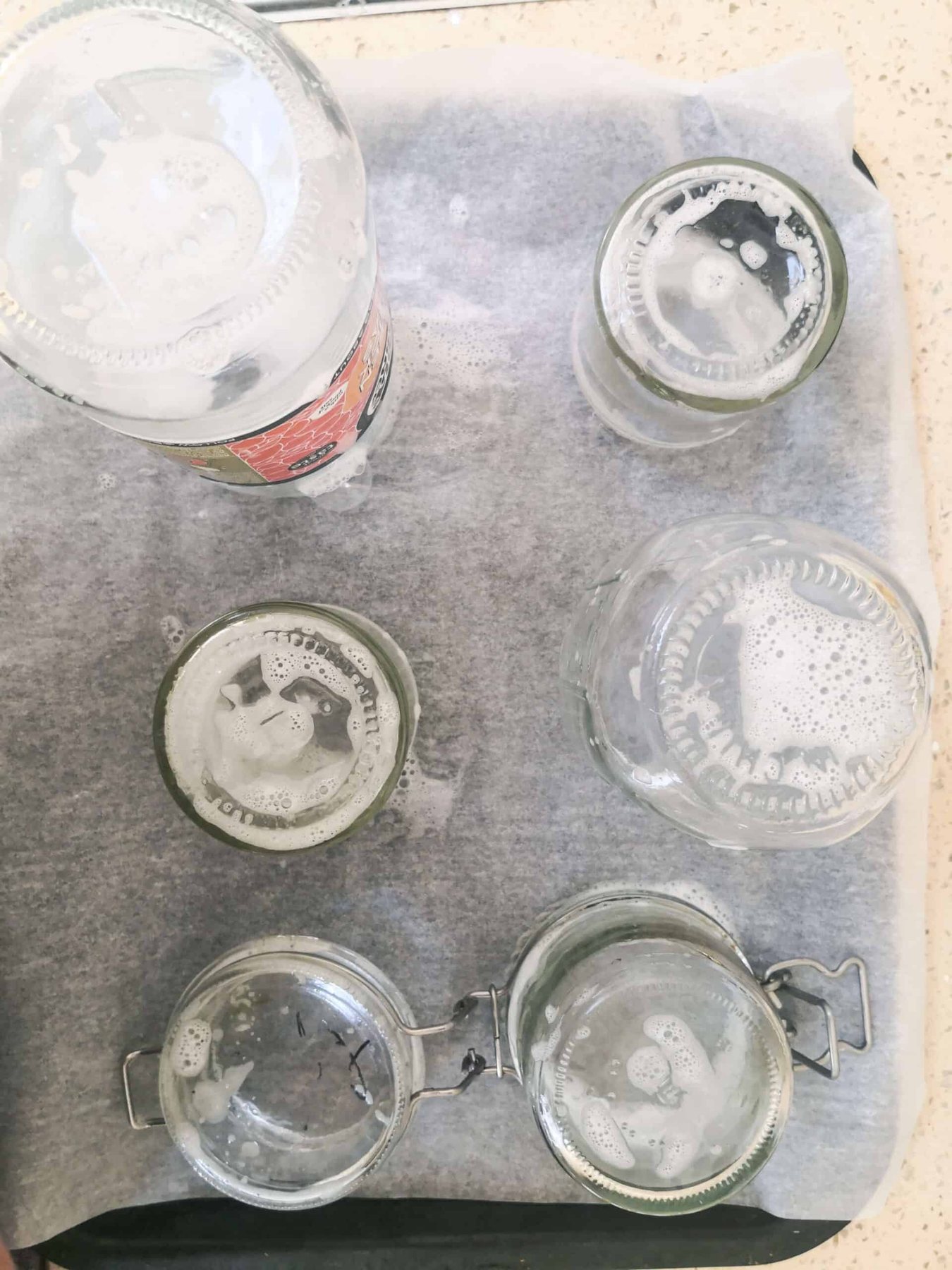 Soapy glass jars standing upright on a lined oven tray.