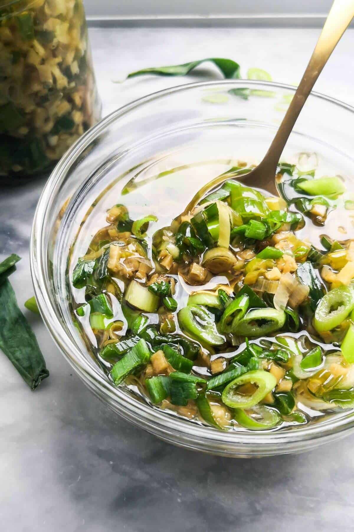 Ginger and spring onion oil in a small glass bowl, with a glass jar of oil in the background.