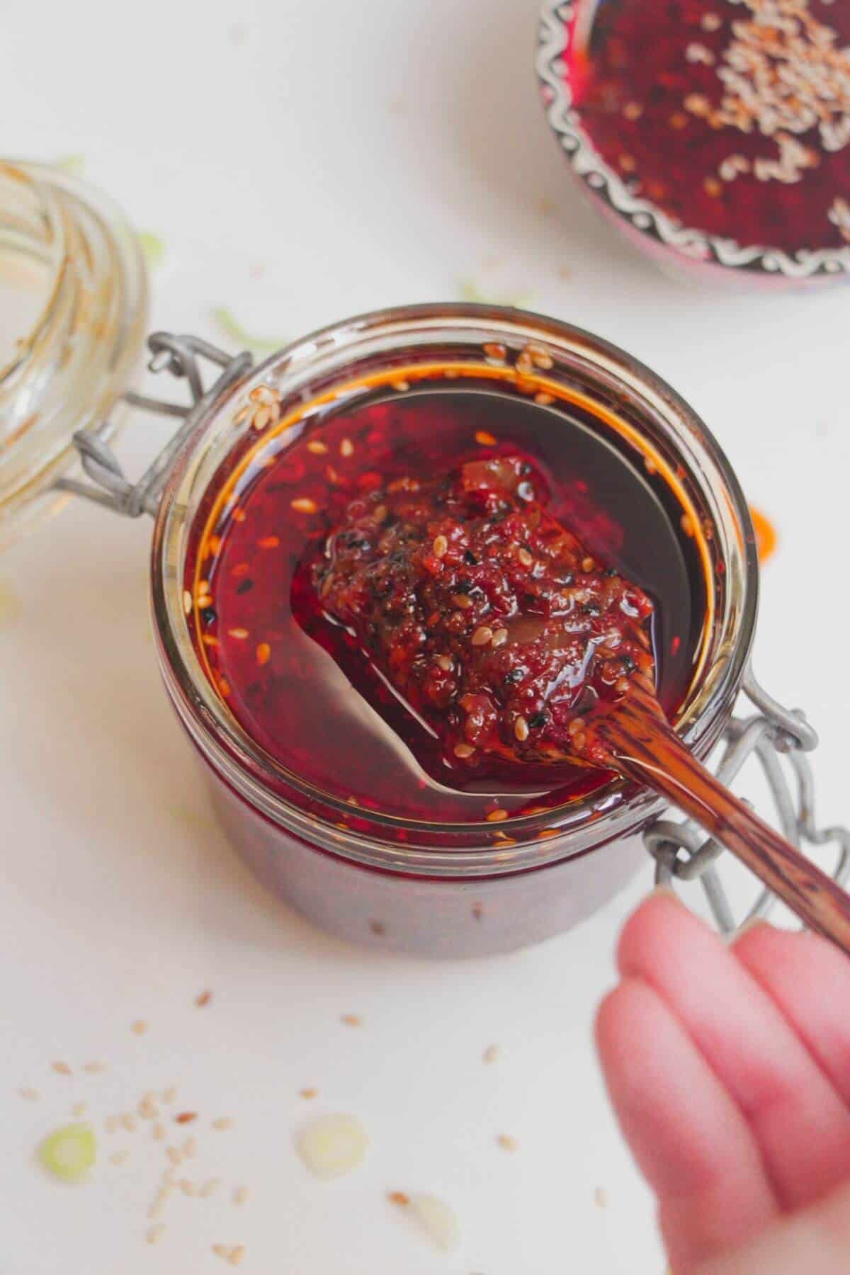Hand holding a wooden spoon with chilli oil on it.