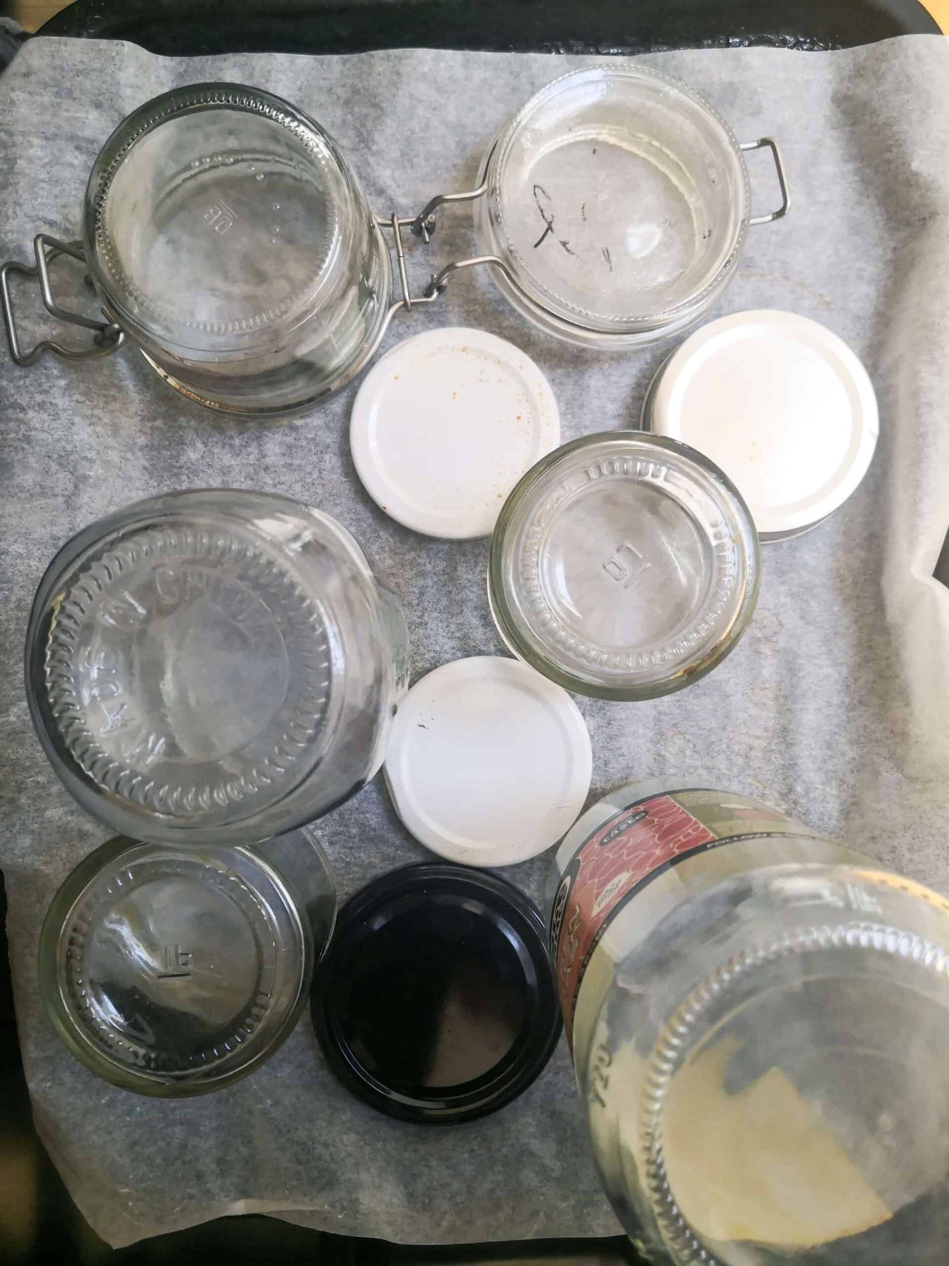 Glass jars standing upside down on a lined oven tray.