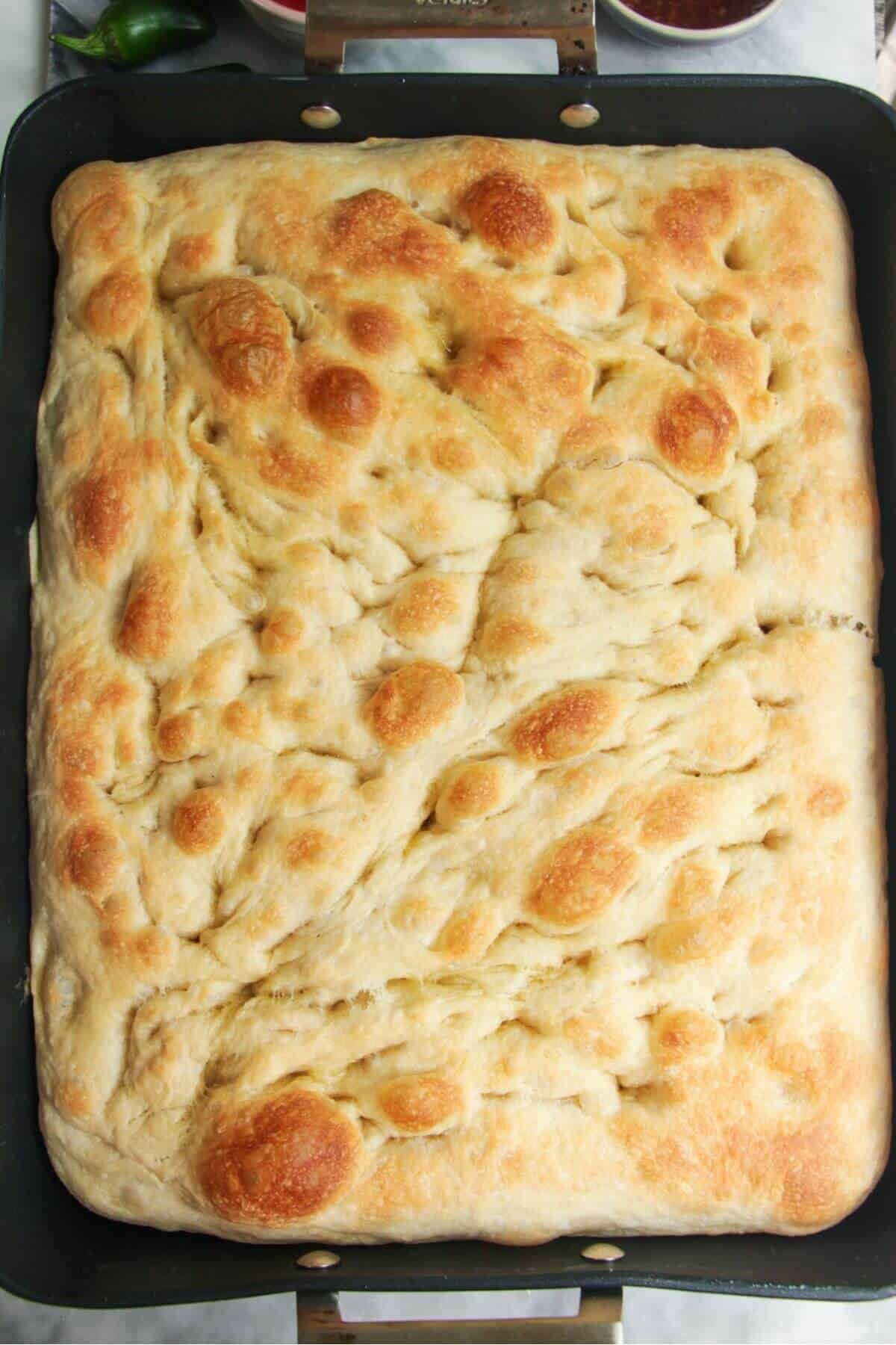 Par-baked focaccia dough in a large oven dish.