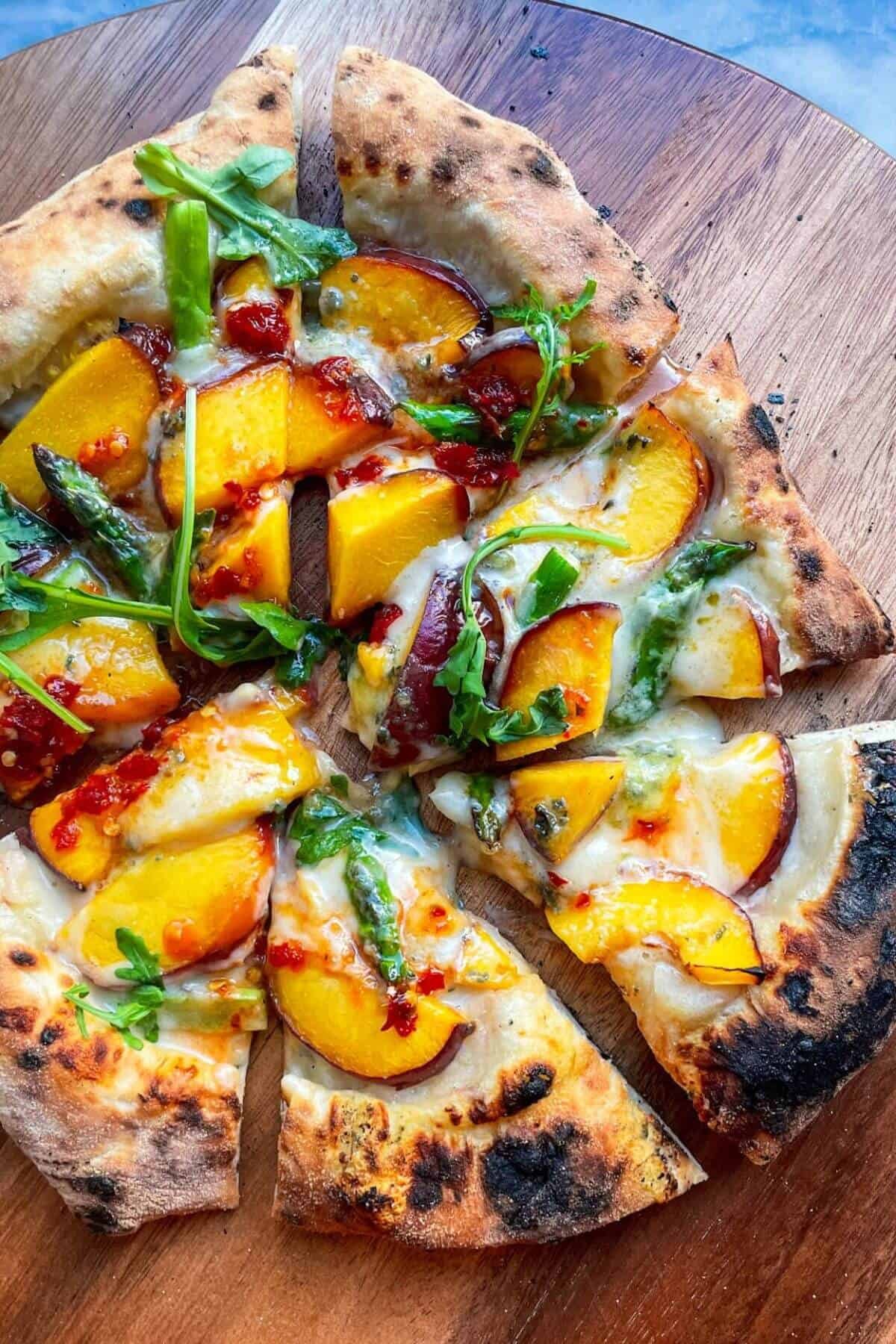Peach blue cheese pizza sliced on a wooden board.