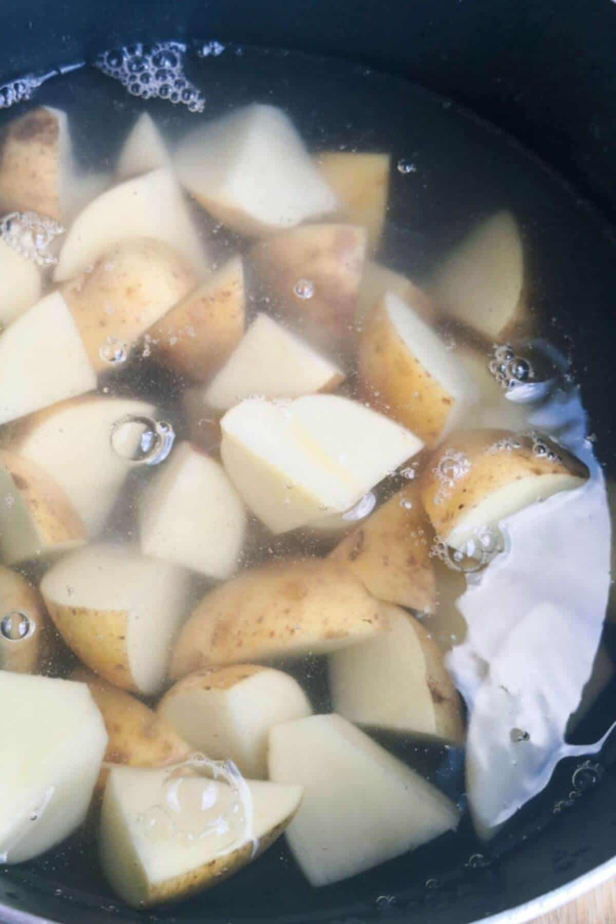 Large black pot of potato chunks covered in water.