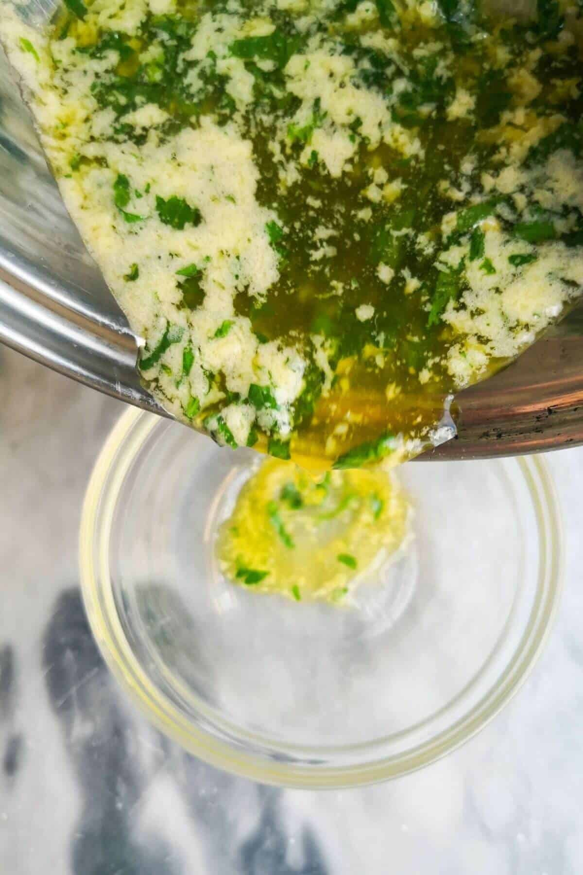 Garlic butter sauce being poured into a small glass bowl from a silver pan.