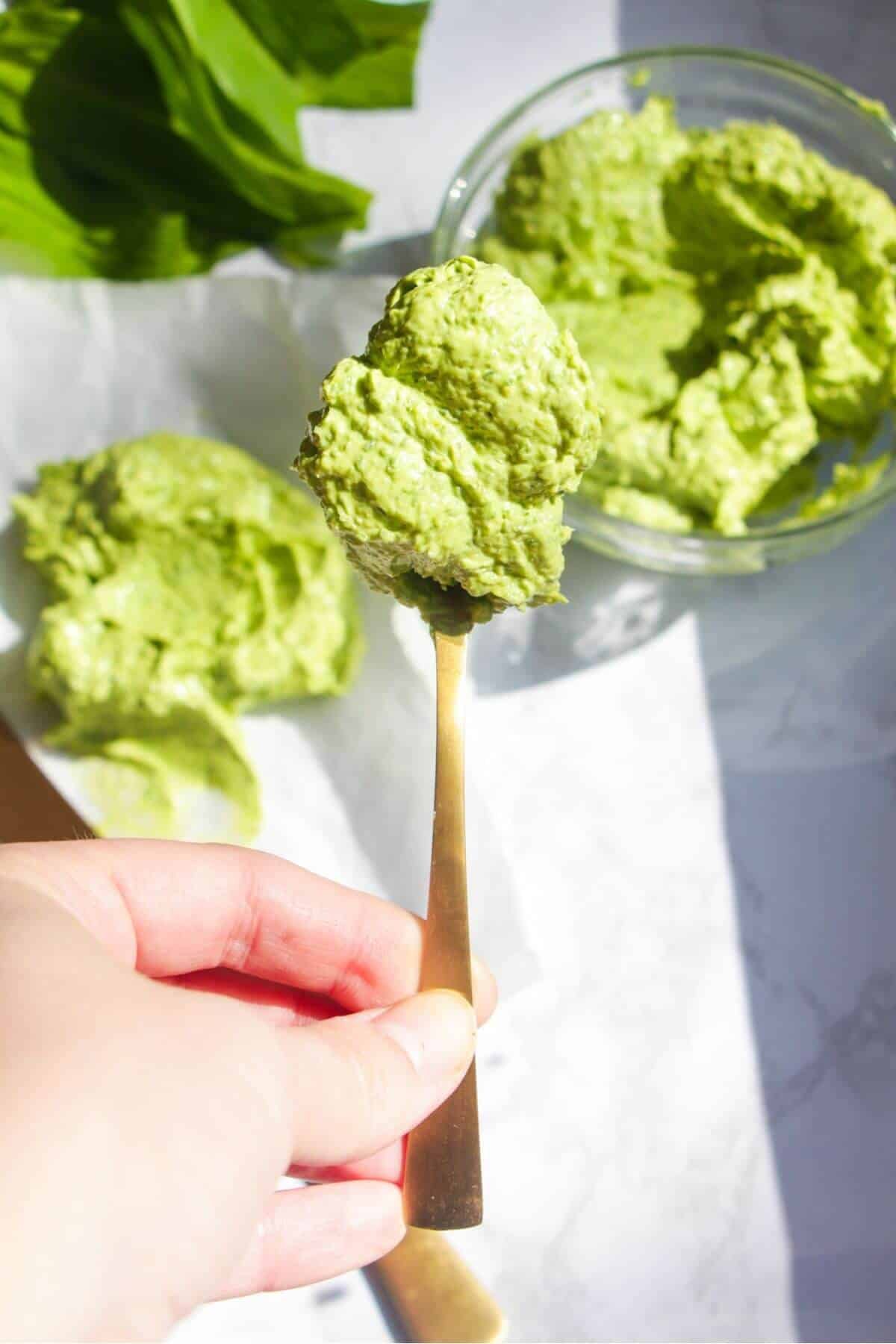 Hand holding up a small gold spoon with wild garlic butter on it.