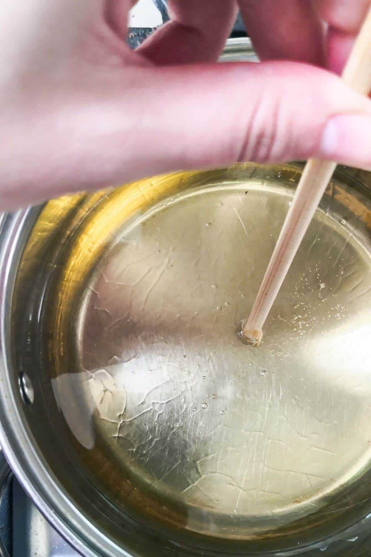 Hand holding wooden chopstick in a pot with oil in it.