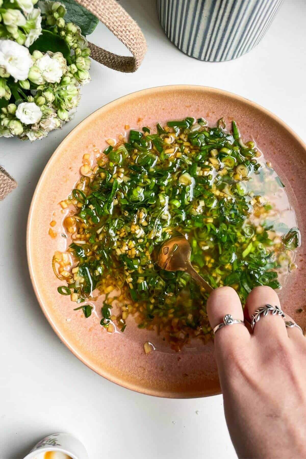 Hand mixing ginger scallion sauce in a shallow bowl.