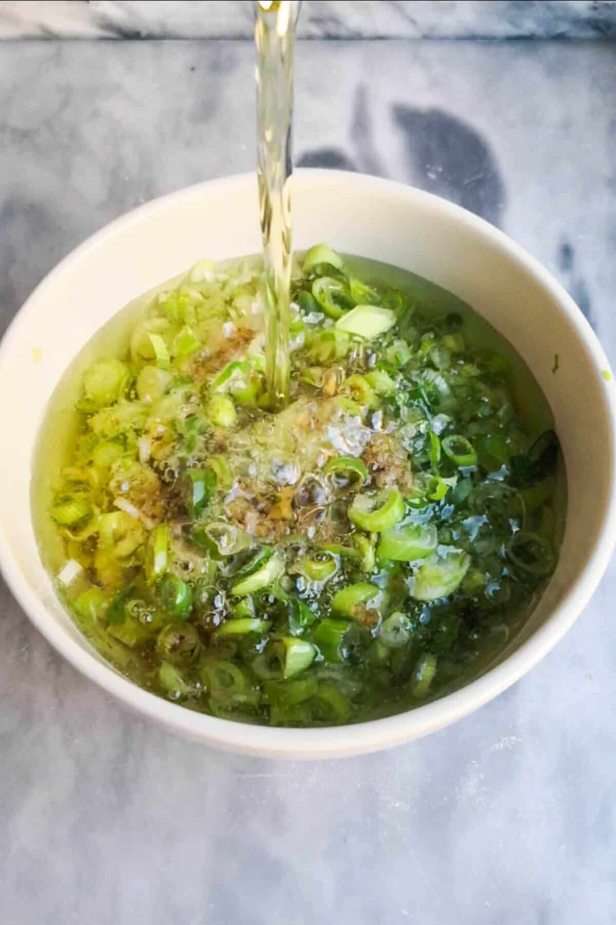 Hot oil being poured into scallions, ginger and soy sauce in a small white bowl.