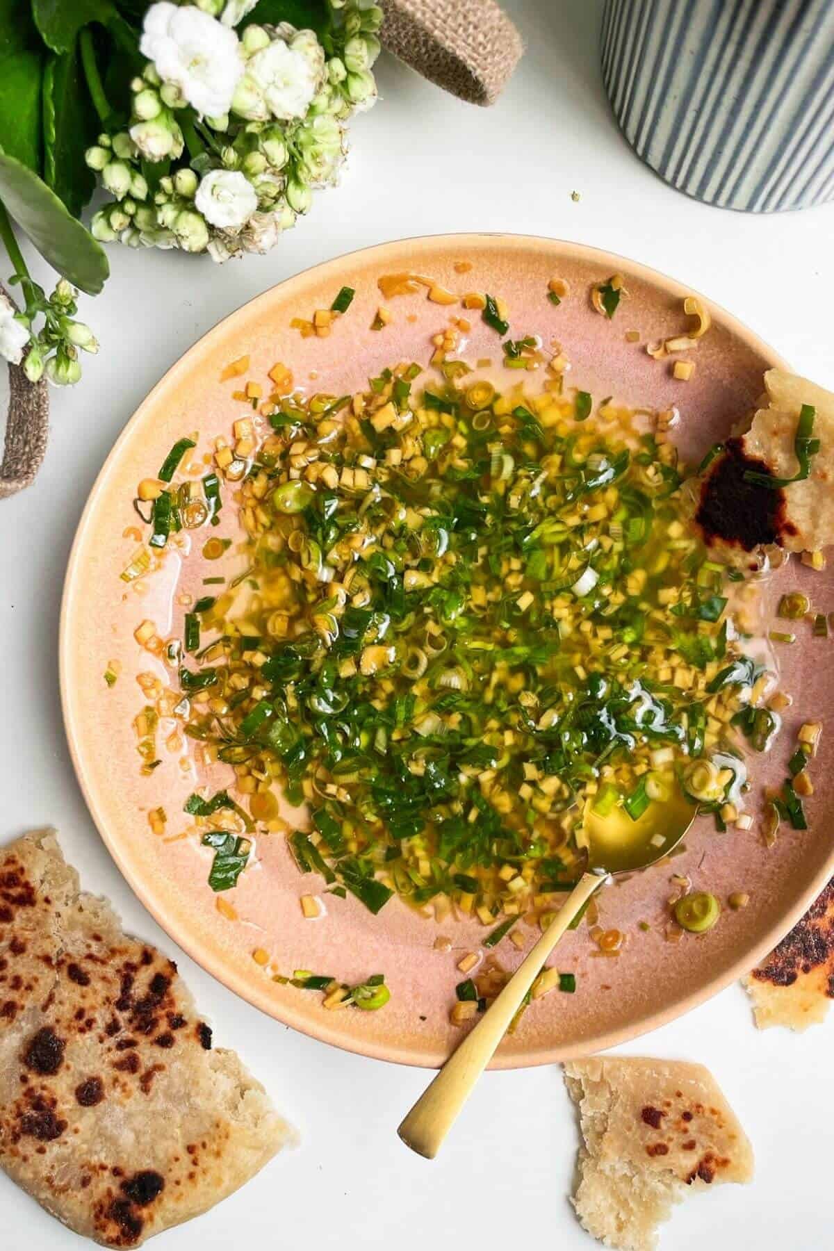 Ginger scallion sauce in a pink bowl with flowers on the side and flatbreads around the bowl.