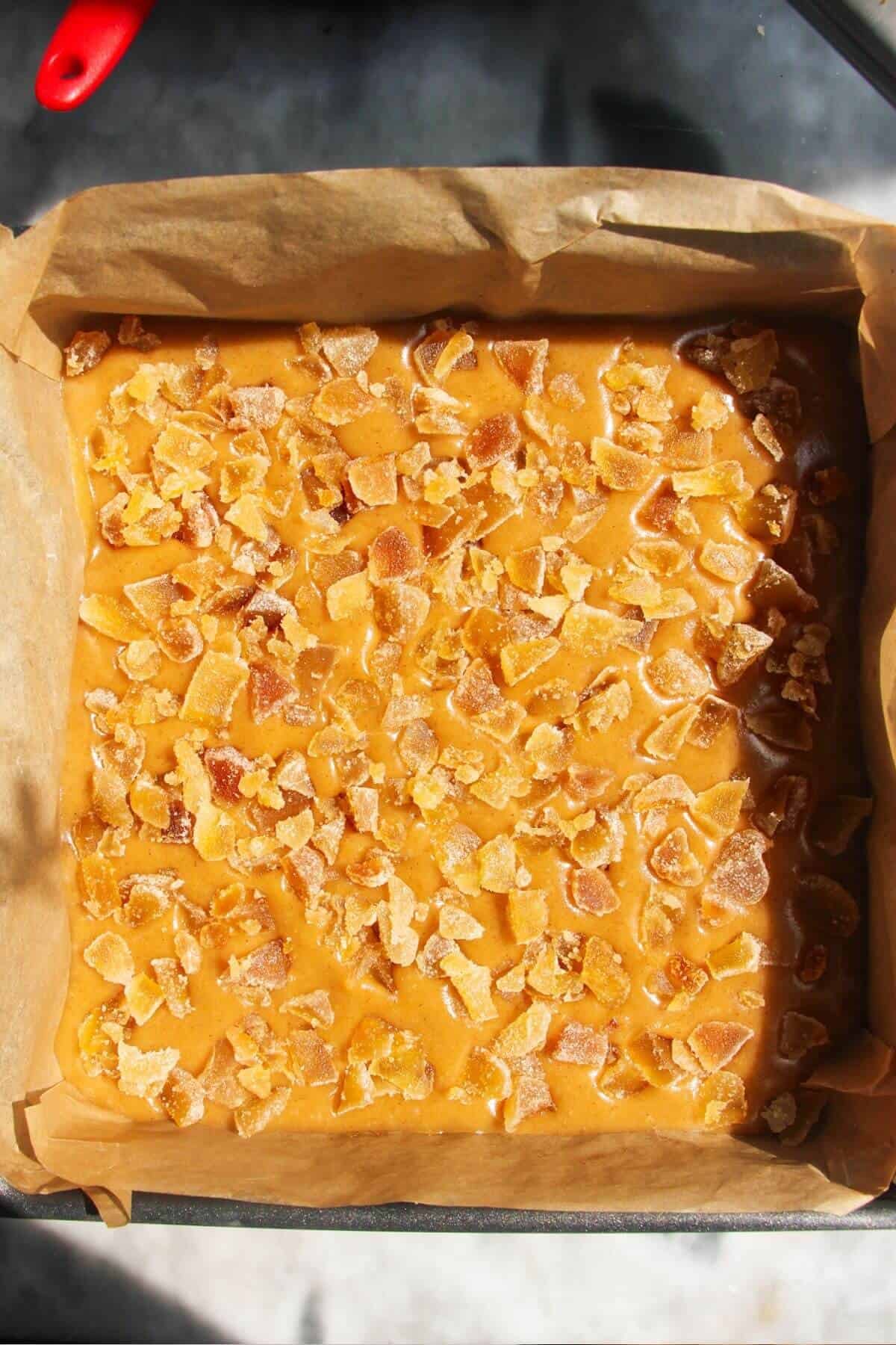 Crystallised ginger scattered on top of ginger icing in a lined baking tin.