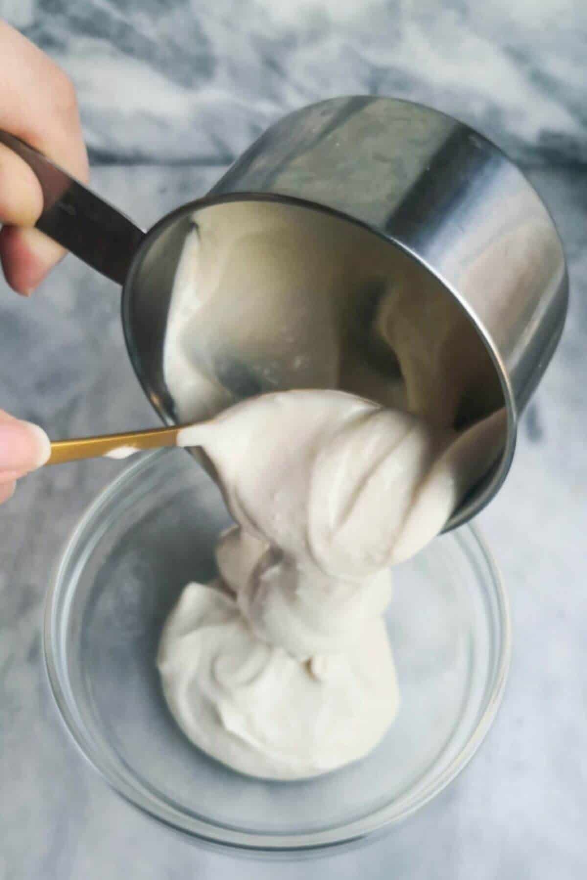 Garlic aioli being added into a small glass bowl with a gold spoon, on a grey marble background.