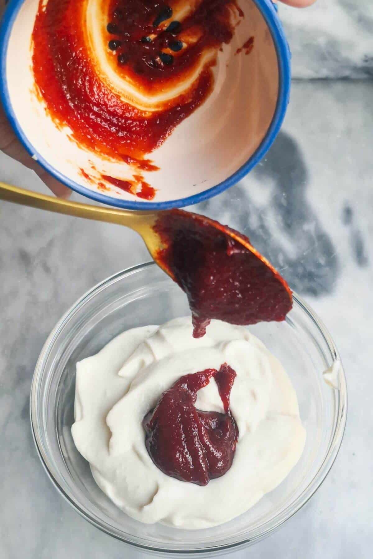 Gochujang paste being added to a small glass bowl with garlic aioli in in.
