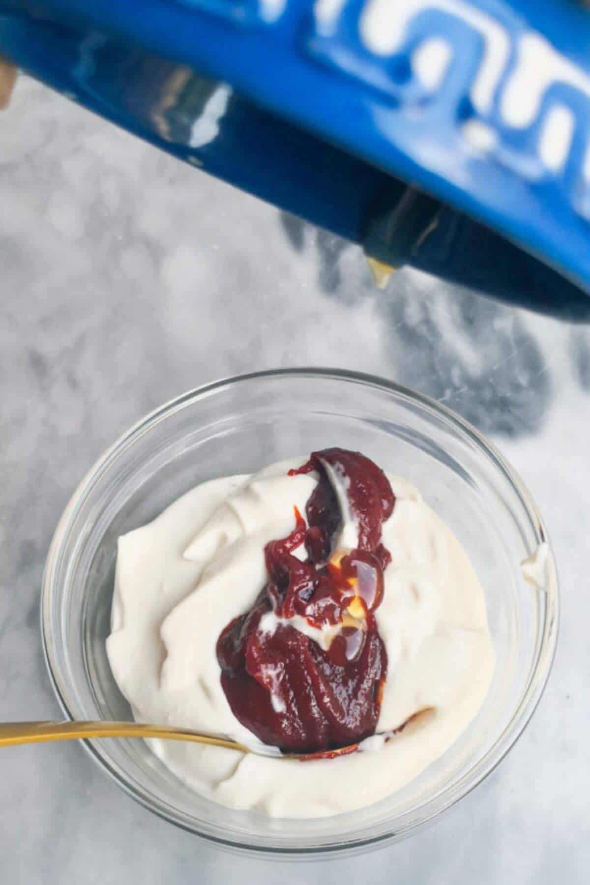 Honey being added to a small glass bowl with garlic aioli and gochujang paste in it.