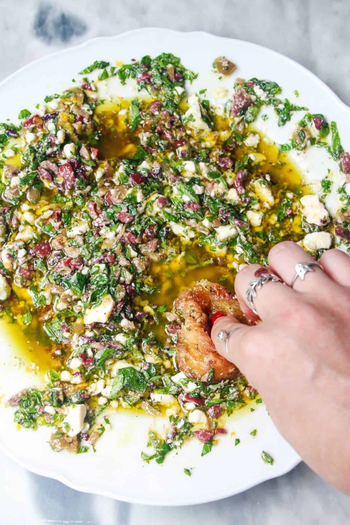 Hand swirling bread through Greek dipping oil in a large white plate.