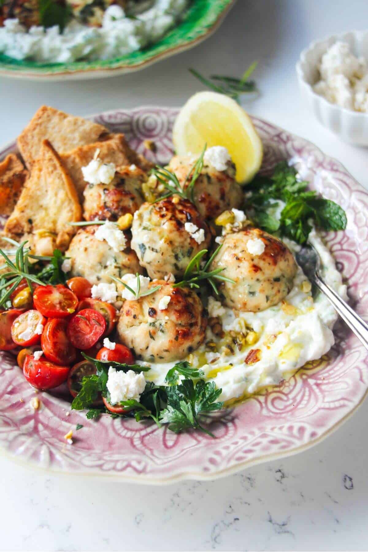 Chicken meatballs, tomatoes, on tzatziki with pita chips on a pink plate.