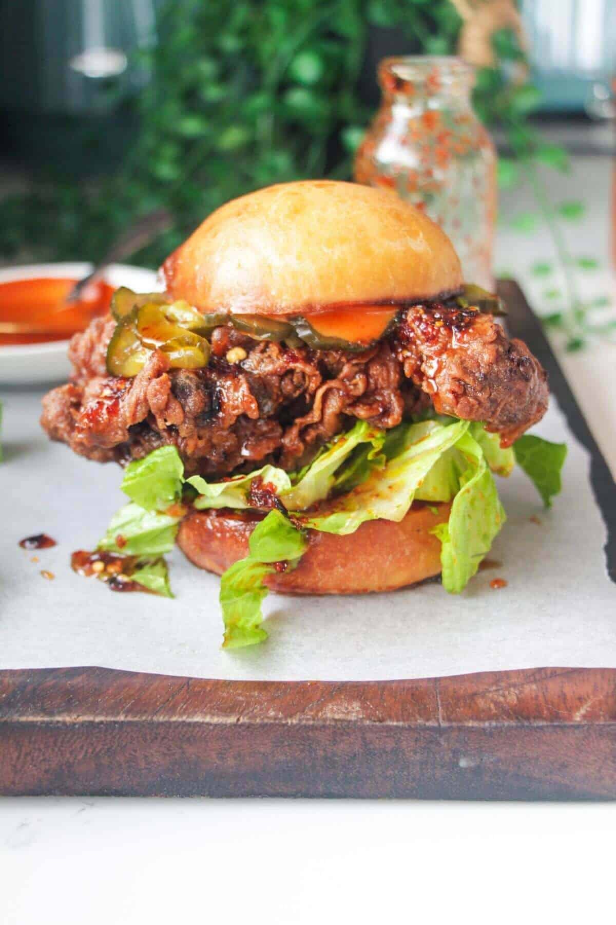 Hot honey fried chicken sandwich on a dark wooden board with small bowl of gochujang aioli in the background.