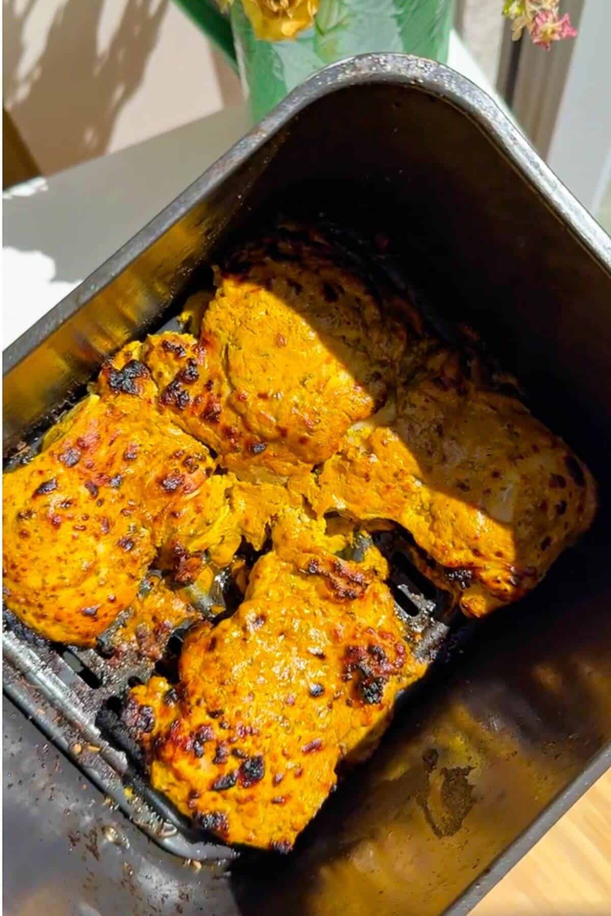 Cooked Greek chicken thighs in air fryer basket.