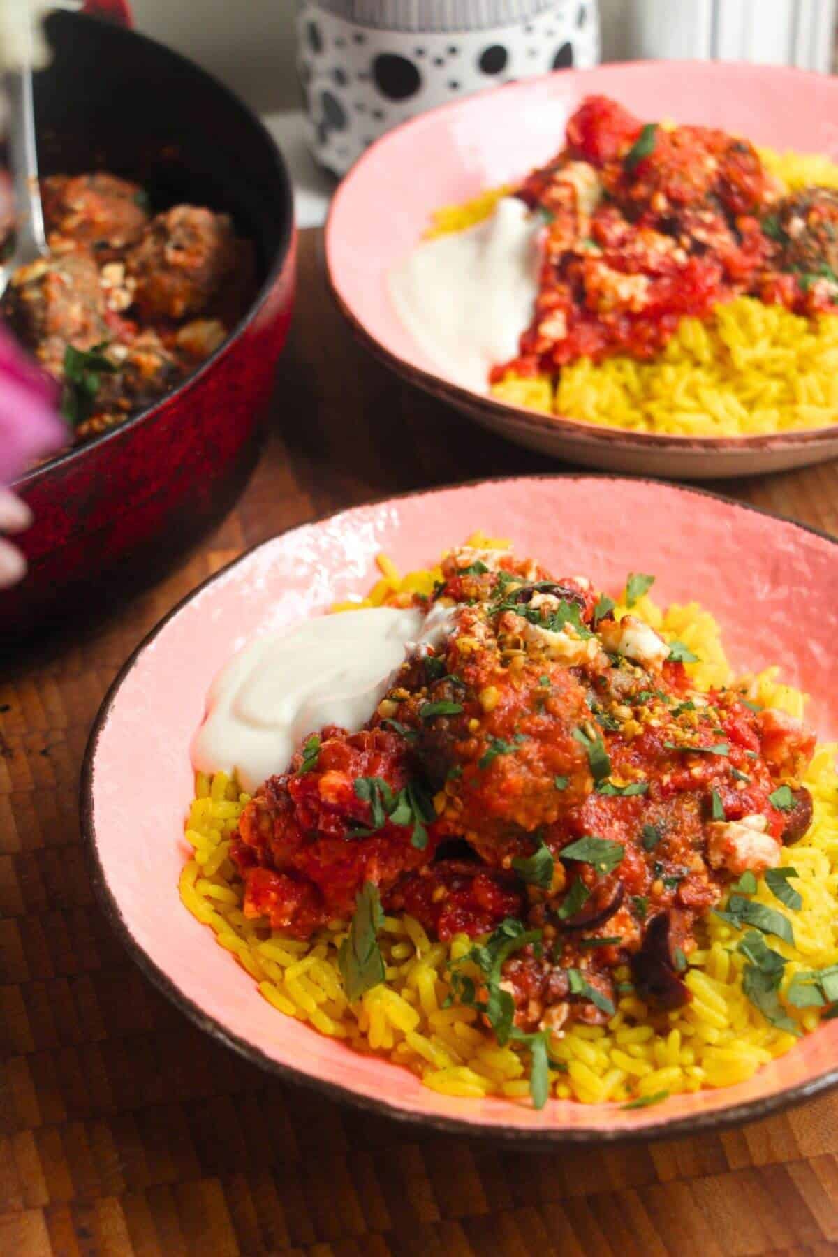 Baked meatballs in tomato sauce on top of golden rice in a pink bowl.