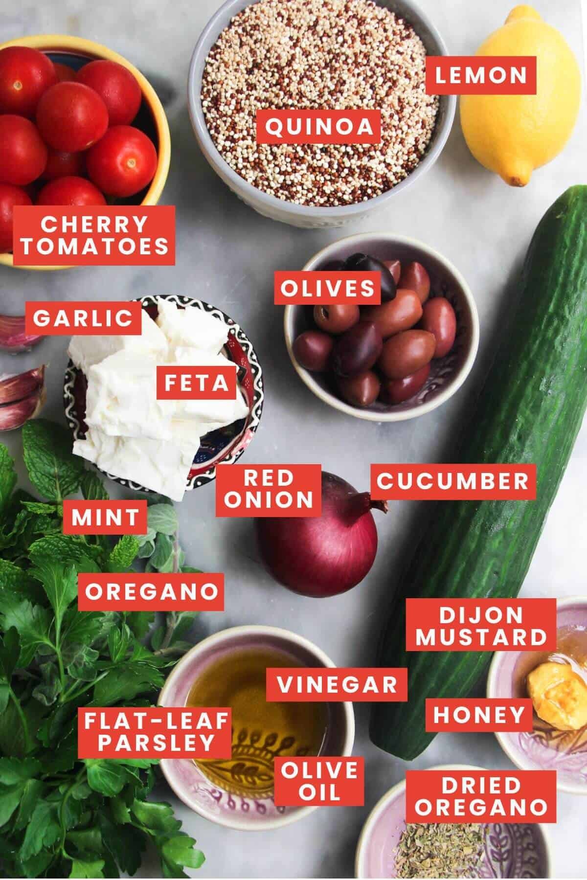 Ingredients for Greek qunioa salad laid out on a marble background and labelled.