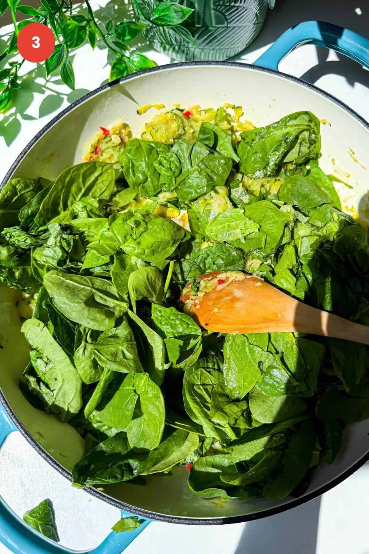 Baby spinach leaves added to greens in a skillet.