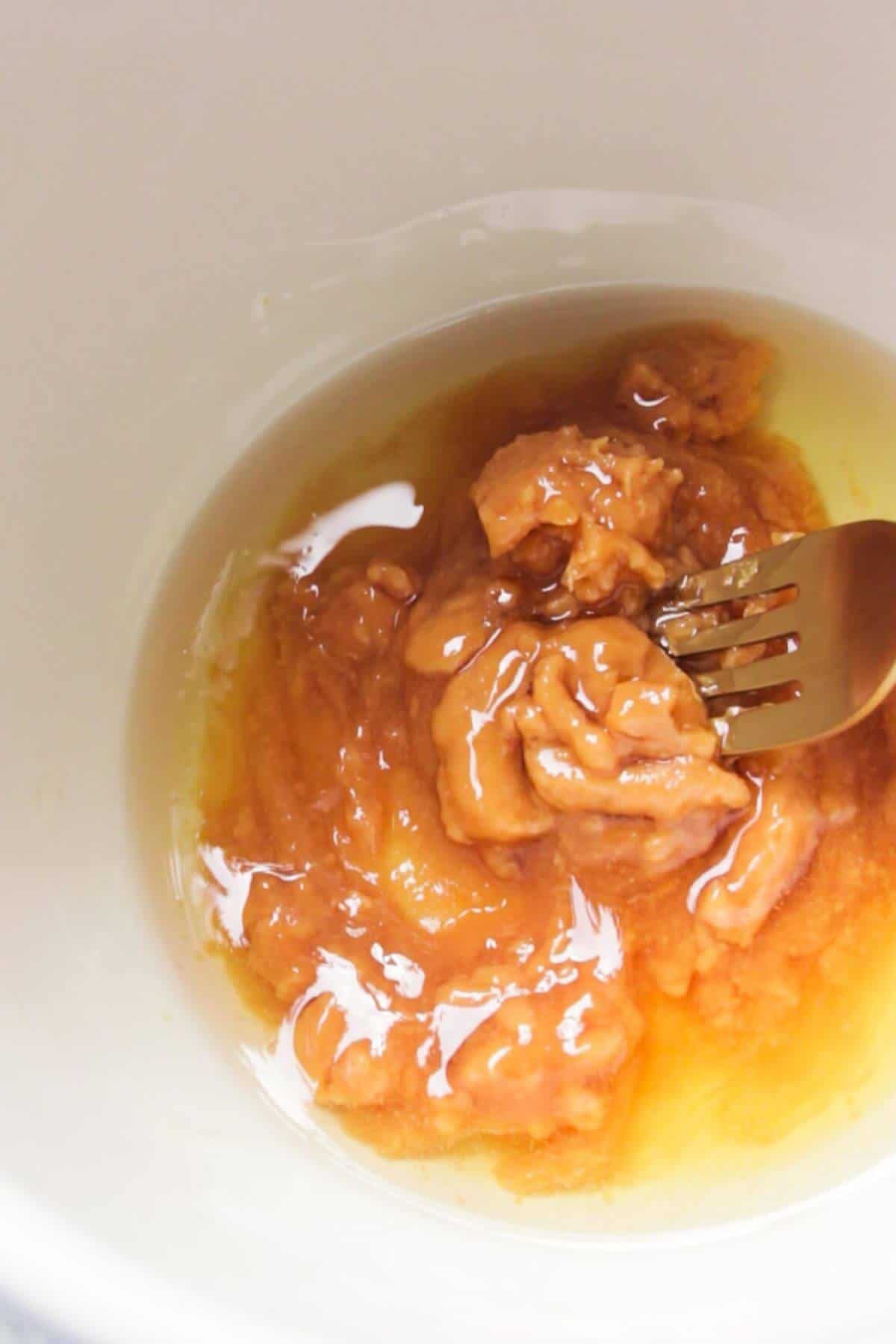 Close up of a gold fork mixing together miso paste, olive oil and honey.