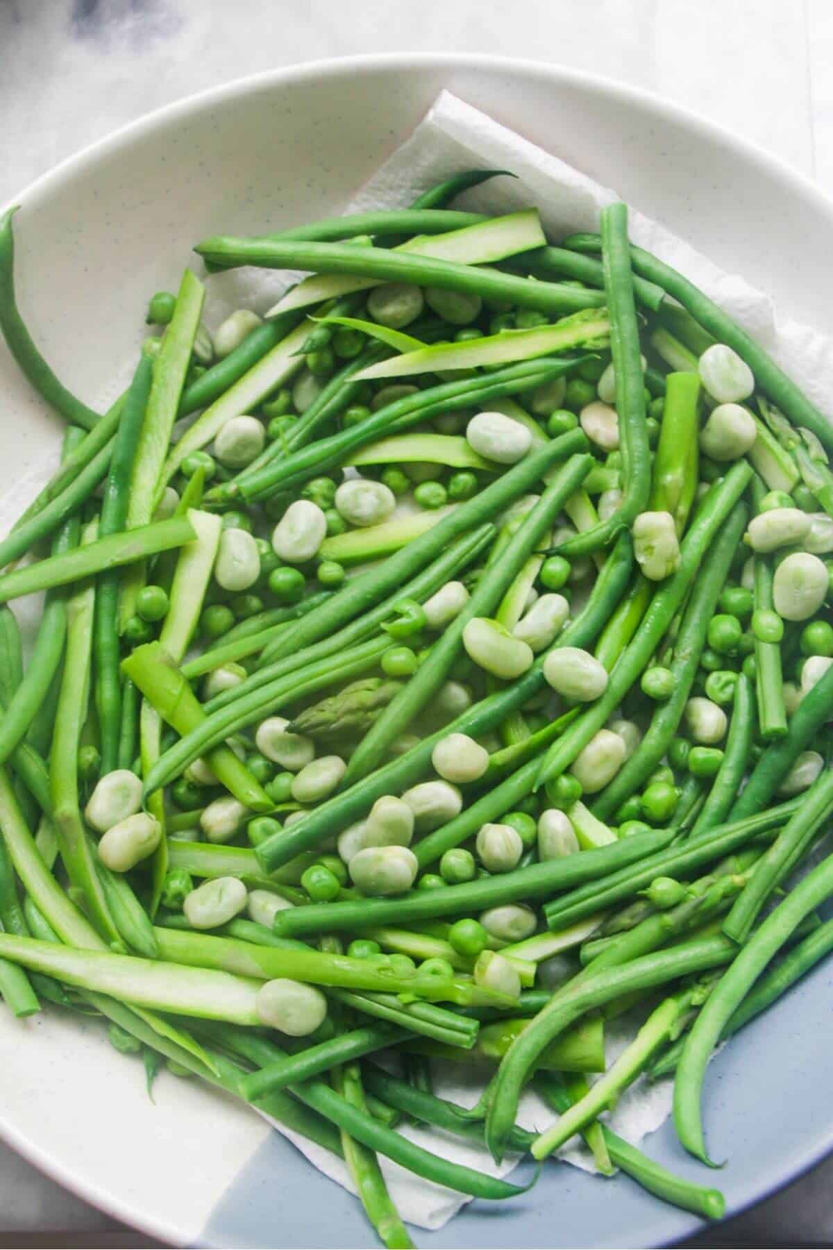 Green beans, asparagus, edamame beans and peas draining in a large serving bowl.