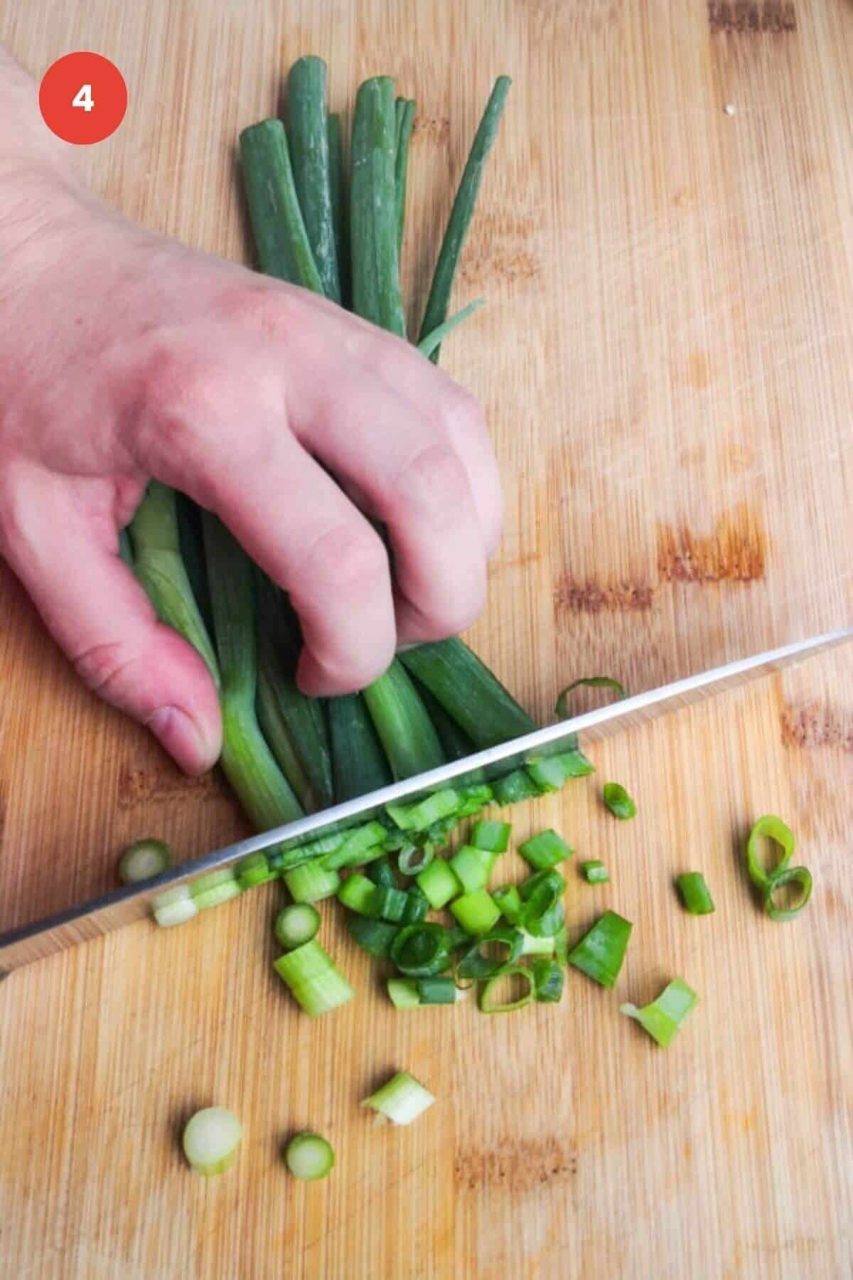 Slicing scallions with a knife on a cutting board.