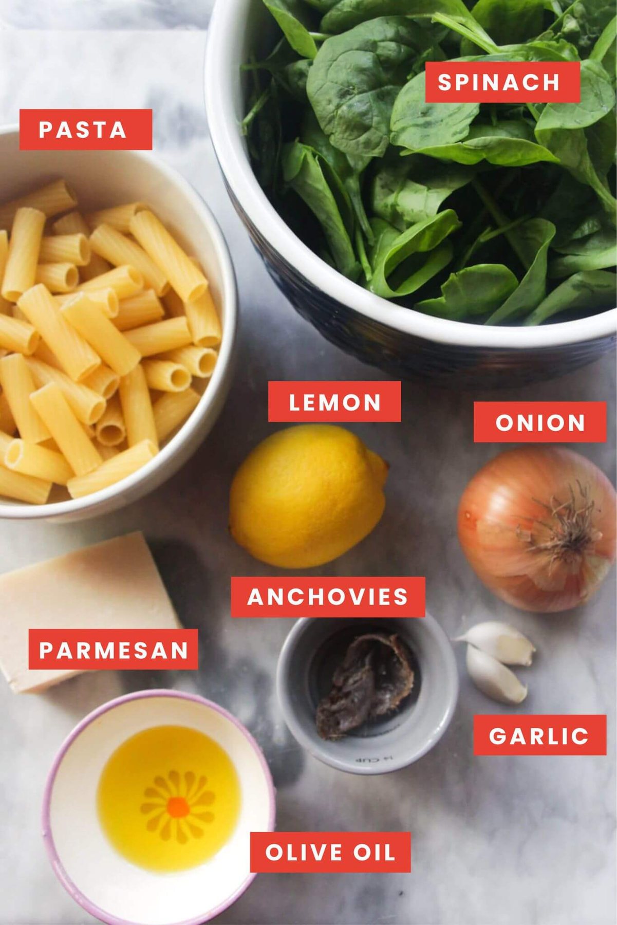 Ingredients for green pasta sauce labelled and laid out on a grey marble background.