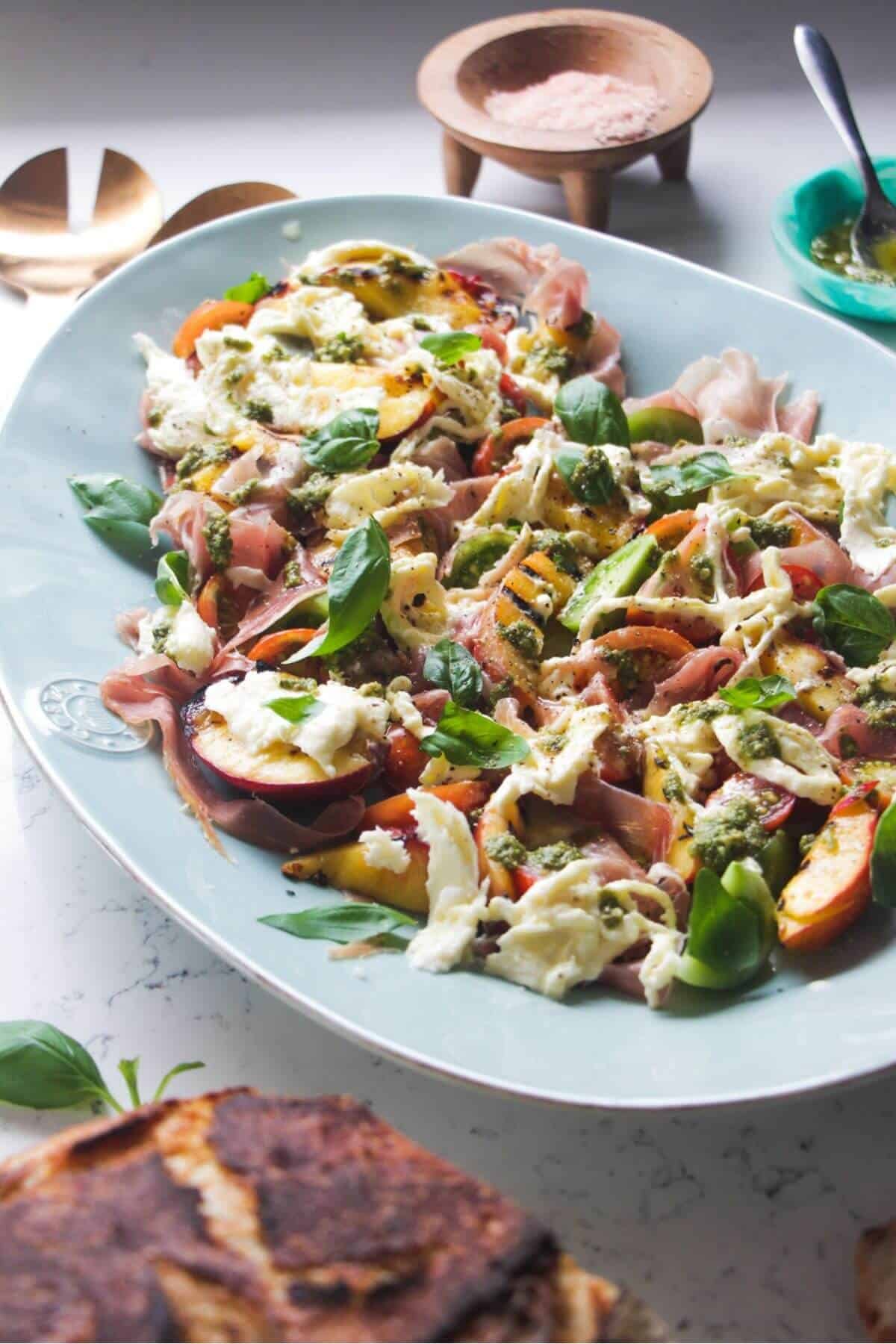 Grilled peach, burrata, tomato salad on a large blue serving platter.