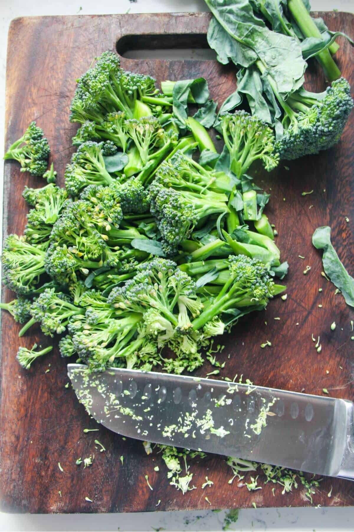 A knife on a wooden board with sliced broccoli.