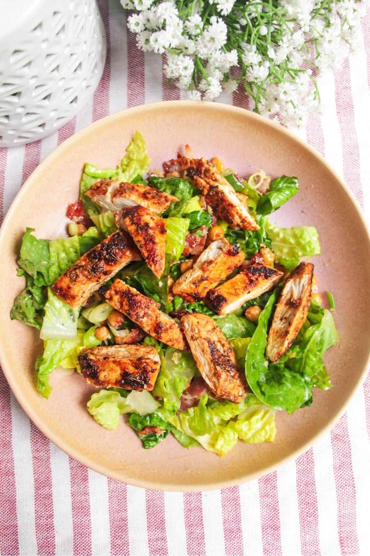 Sliced chicken on top of lettuce in a pink bowl.