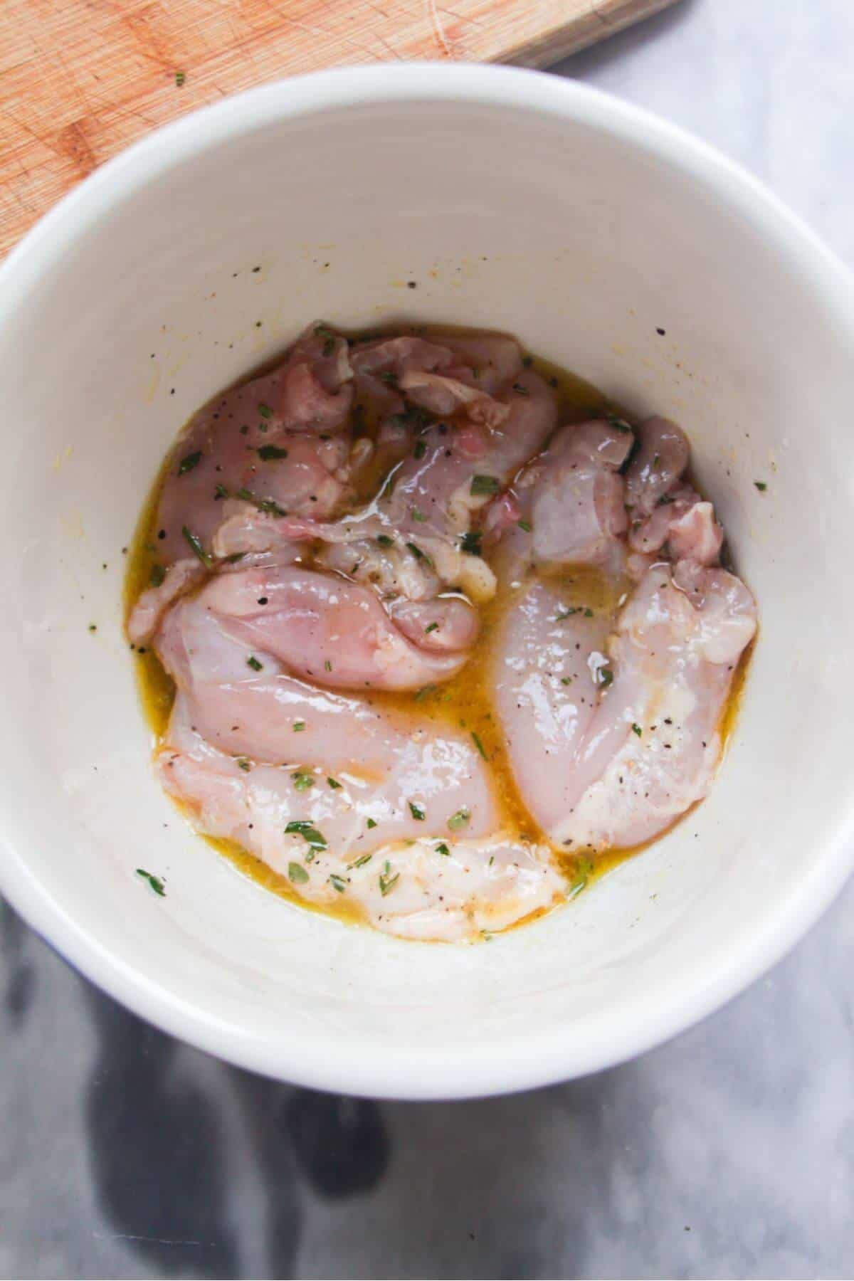 Chicken thighs marinating in a small white bowl.