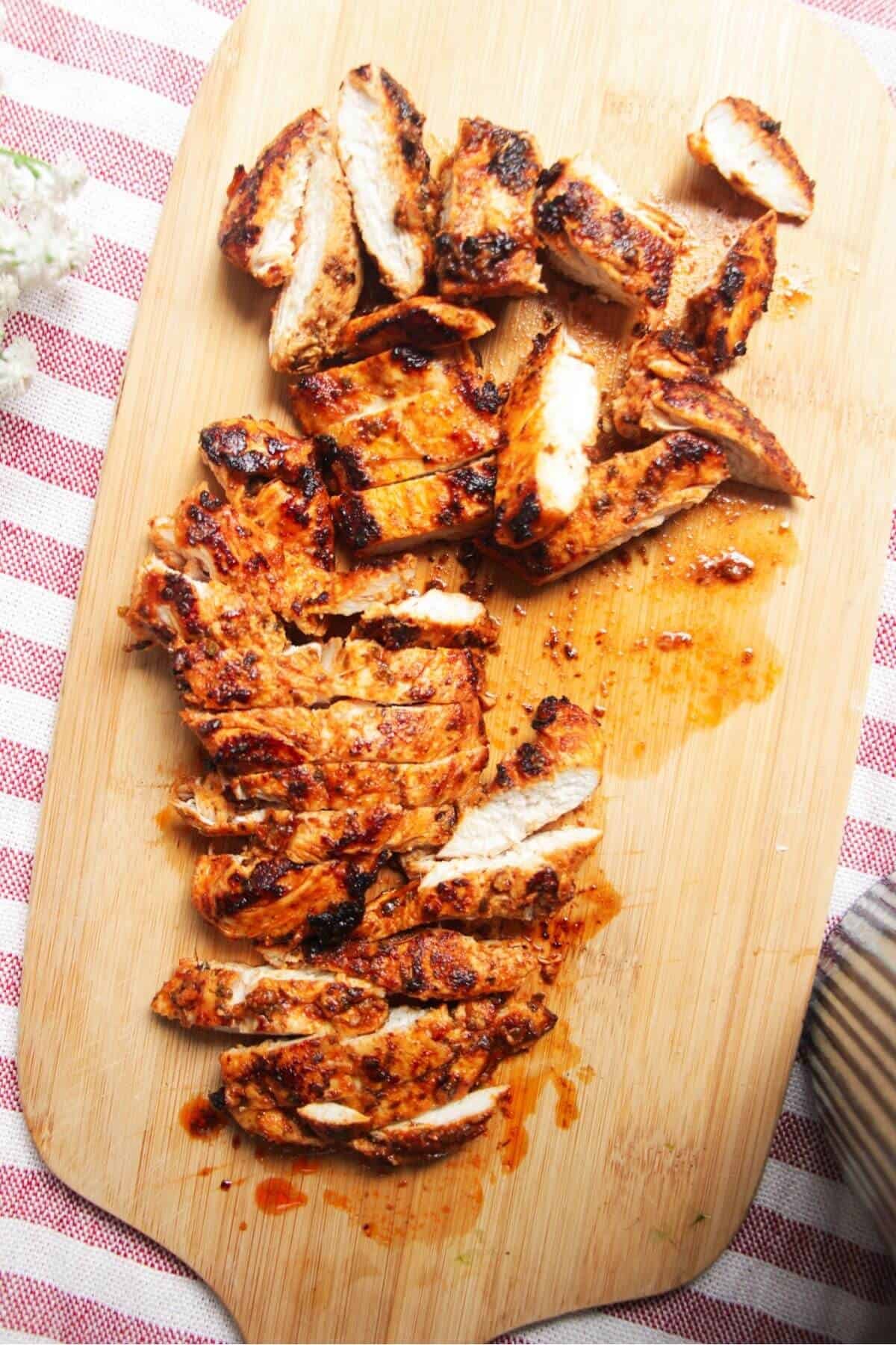 Sliced charred chicken on a wooden board.