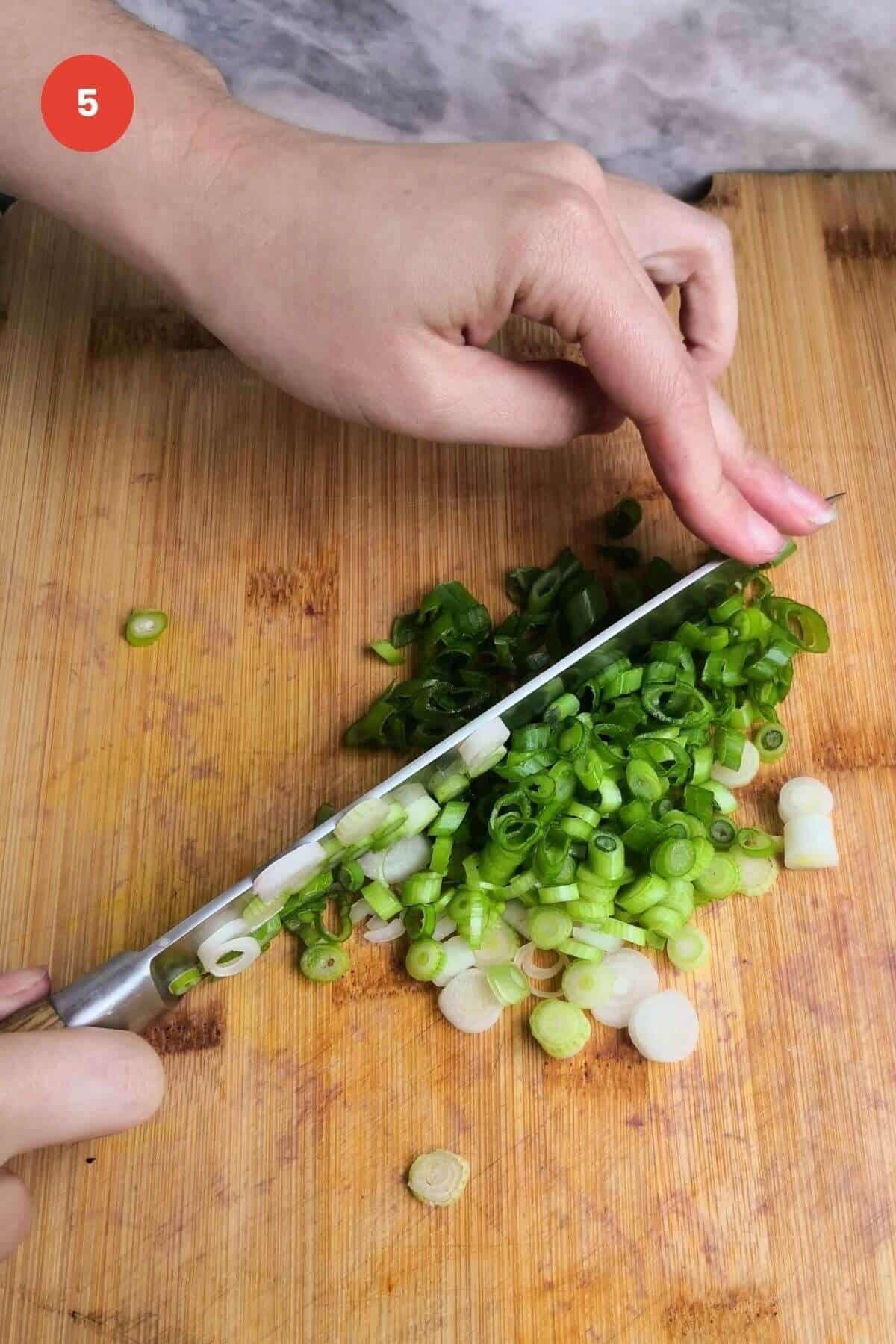 Slicing scallions with a knife on a cutting board.