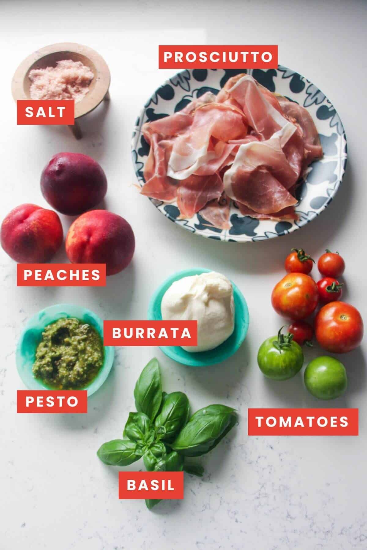 Ingredients for grilled peach burrata salad on a white marble background and labelled.