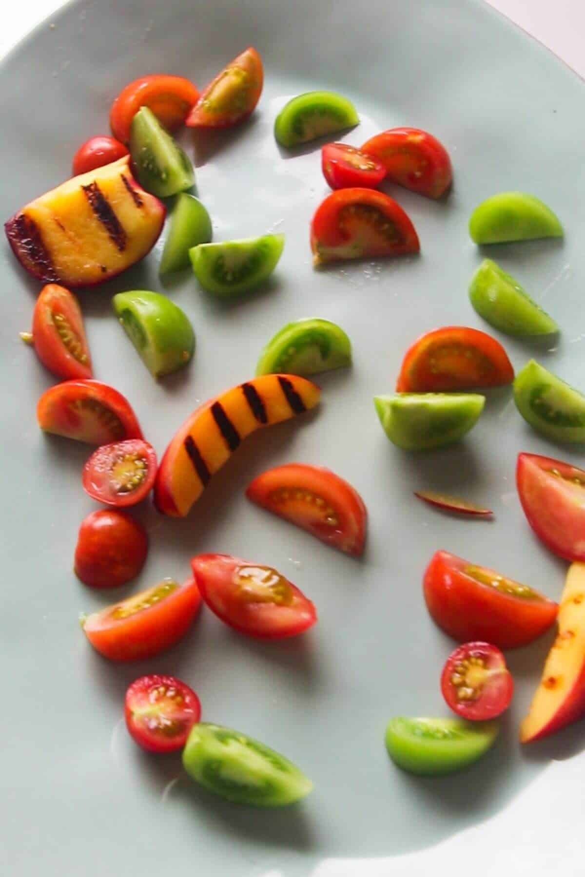 Sliced tomatoes and grilled peaches laid out on a large pale blue oval plate.