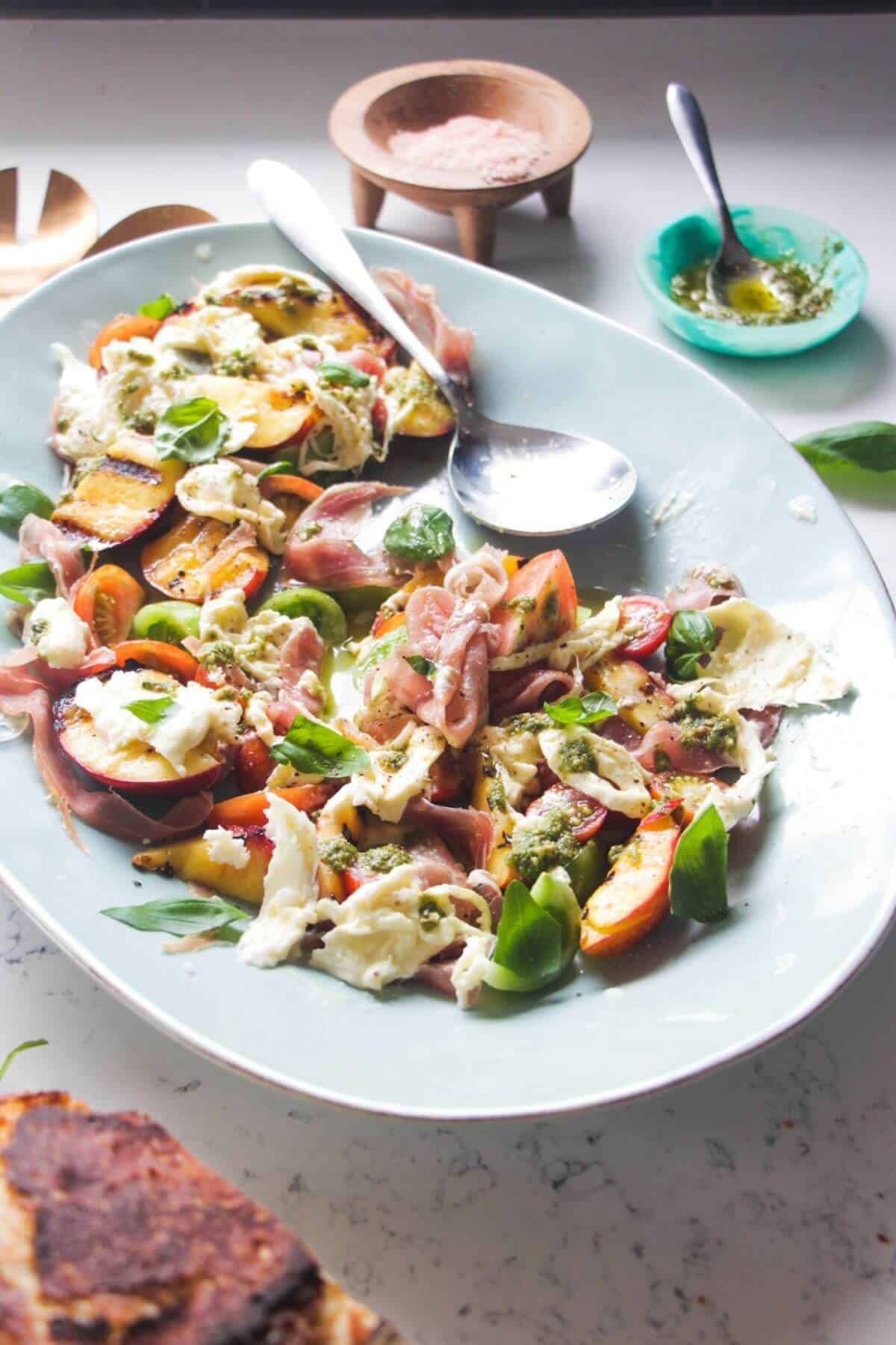 Grilled peach and burrata salad with a silver spoon on the plate.