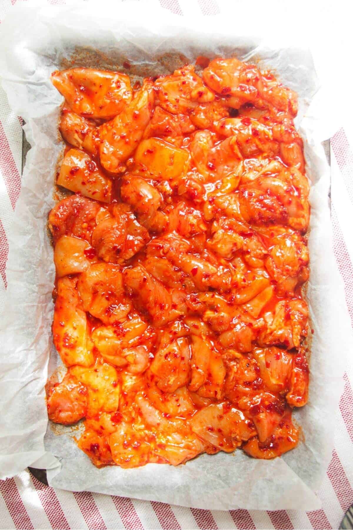Diced marinated chicken on a lined oven tray.