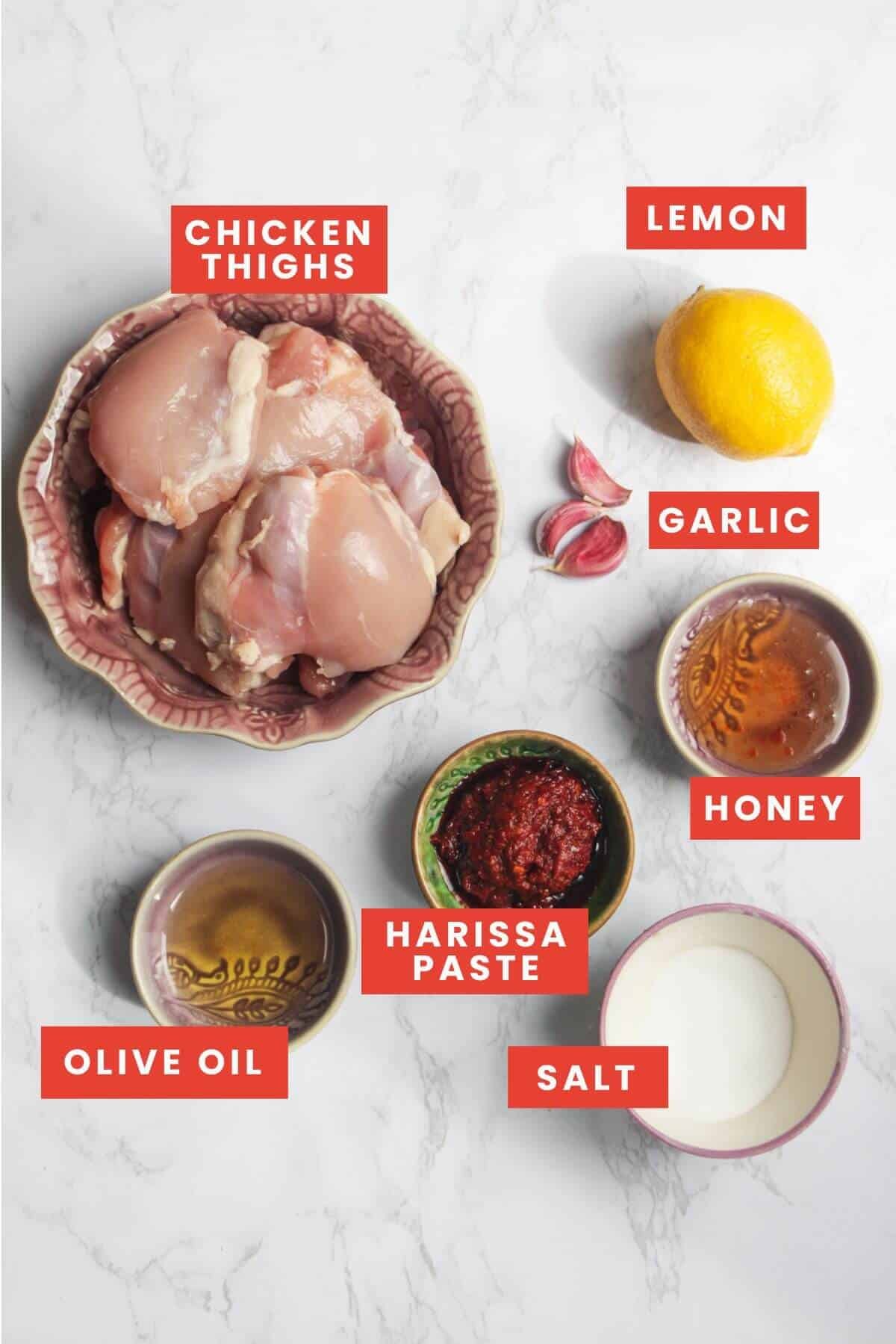 Harissa honey chicken ingredients laid out on a white marble background and labelled.