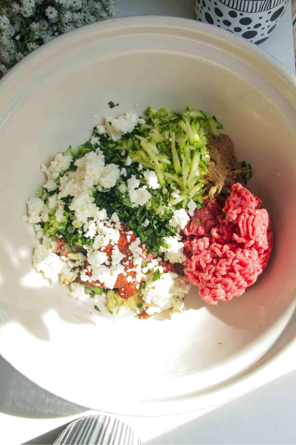Ingredients for harissa, feta and zucchini meatballs in a large mixing bowl.