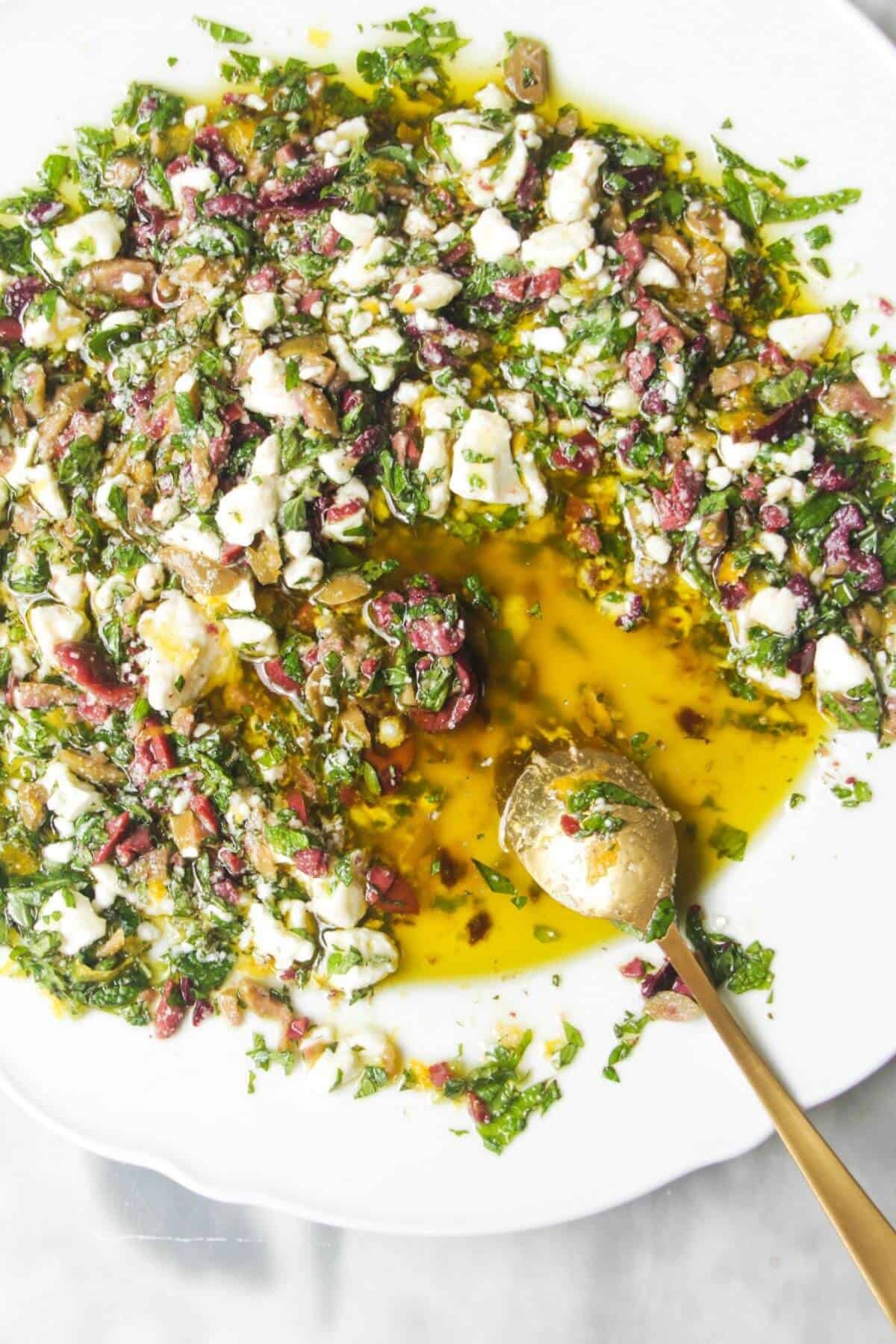 Small gold spoon in Greek style bread dipping oil in a large white plate.
