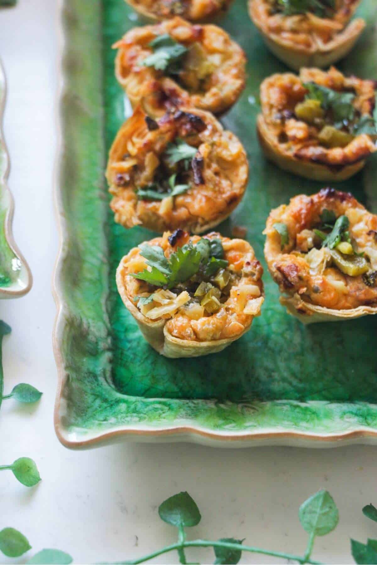 Jalapeno popper taco cups on a green rectangular plate, with a bowl of jalapenos on the side.