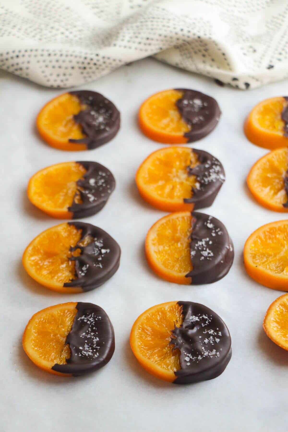 Dark chocolate dipped candied orange slices laid out on a baking paper lined tray.