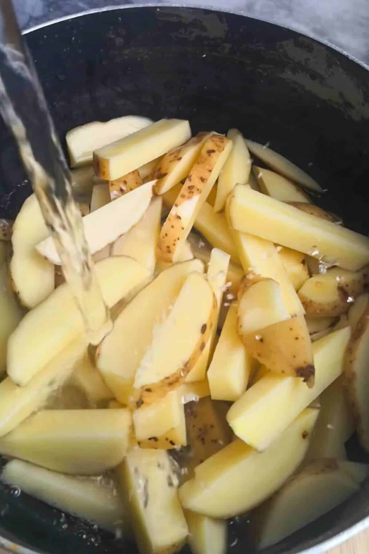 Water being poured into a large black pot filled with chips.
